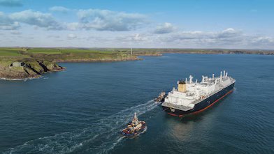Cargo ship in the middle of water passing land.